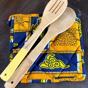 May include: Two wooden spoons with yellow and brown handles on a blue and yellow quilted hot pad. The hot pad has a geometric pattern with yellow clouds on a blue background.