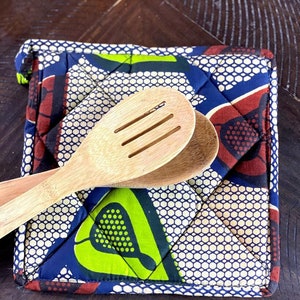May include: A blue, green, and brown quilted hot pad with a geometric pattern. Two wooden spoons are on top of the hot pad.