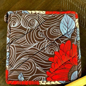 May include: A brown quilted hot pad with a red, blue, and white floral pattern. The pattern features large red flowers with white centers and blue leaves.