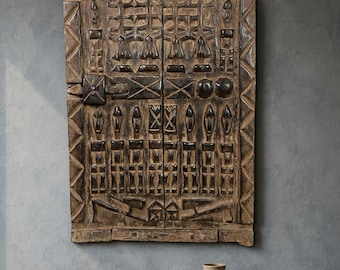 May include: A dark brown wooden desk with two drawers, a matching chair with a woven cane back and seat, and a large, rectangular, intricately carved dark wood wall panel featuring geometric patterns and raised relief details.
