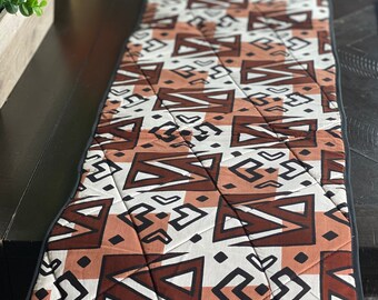 Peut inclure: Un chemin de table matelassé avec un motif géométrique brun, blanc et noir et une bordure noire. Le motif est en forme de losange.