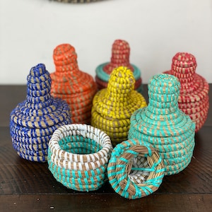 May include: A set of colorful woven baskets with lids. The baskets are made of natural materials and have a unique, hand-crafted look. The baskets are available in a variety of colors, including blue, yellow, orange, and red.
