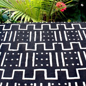K&ouml;nnte beinhalten: Schwarz-wei&szlig; gemusterter Stoff mit geometrischem Design. Der Stoff zeigt wei&szlig;e Linien, Quadrate und Punkte auf schwarzem Hintergrund.