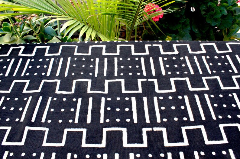K&ouml;nnte beinhalten: Schwarz-wei&szlig; gemusterter Stoff mit geometrischem Design. Der Stoff zeigt wei&szlig;e Linien, Quadrate und Punkte auf schwarzem Hintergrund.