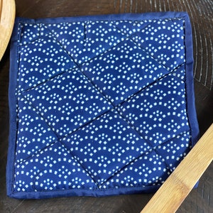May include: A blue quilted hot pad with a white geometric pattern. The pad is made of cotton and is perfect for protecting surfaces from hot dishes.