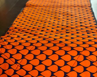 Peut inclure: Un tissu matelassé orange et bleu marine, orné d'un motif répétitif en forme de goutte d'eau. Le tissu est posé sur une surface sombre, mettant en valeur le motif géométrique. Le matelassage ajoute de la texture et de la profondeur au textile.