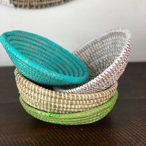 May include: Three woven baskets, one turquoise, one natural, and one white, are stacked on top of each other. The baskets are made of natural materials and have a woven pattern.