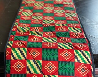 Peut inclure: Un chemin de table rouge, vert et or avec un motif géométrique. Le chemin de table est matelassé et a une bordure noire.