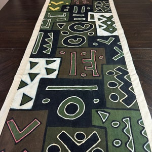 Może przedstawiać: Czarno-zielony bieżnik stołowy z białą obwódką. Bieżnik zdobi geometryczny wzór z kół, trójkątów i kwadratów w odcieniach zieleni, czerni i bieli.