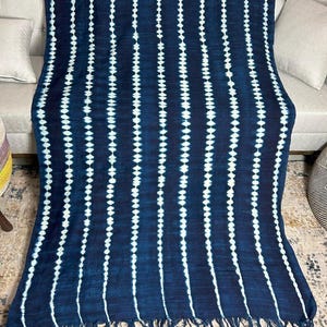 May include: A dark blue textile with vertical white dotted lines and fringed edges. The fabric is draped over a sofa, showcasing its texture and pattern. This decorative throw blanket adds a touch of bohemian style to any living space.