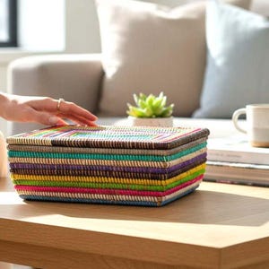 May include: A multi-coloured rectangular woven storage box with a lid. The box has horizontal stripes in shades of brown, teal, yellow, pink, and blue. The box is on a wooden table.