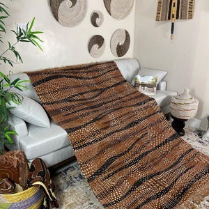 May include: A brown and black patterned textile with a fringed edge is draped over a gray sofa. Woven wall decor in various sizes and shapes adorns the wall. A decorative basket and other items are visible in the foreground.