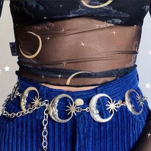 May include: A silver chain belt with crescent moon and star charms. The belt is worn over a blue denim skirt.