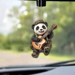 May include: A black and white panda bear figurine playing a brown guitar. The panda is wearing a green and brown vest and a brown hat. The figurine is attached to a silver chain.