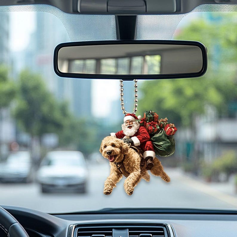 May include: A red and white Santa Claus riding a brown dog with a green bag of presents hanging from his arm. The ornament is hanging from a rearview mirror in a car.