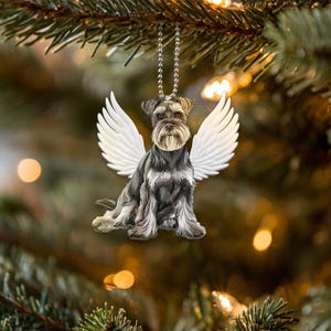 Può includere: Uno schnauzer nano nero e grigio con ali d'angelo bianche, un ornamento natalizio.