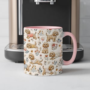 Pode incluir: Uma caneca de cerâmica com asa e rebordo interior cor-de-rosa claro, com um padrão repetitivo de cães castanhos claros de pelo encaracolado a usar várias camisolas e camisas estampadas, intercaladas com pequenas ilustrações florais.