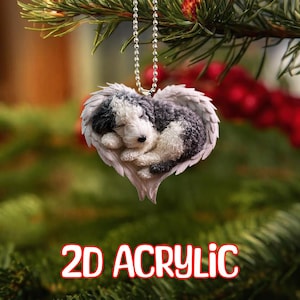 May include: A 2D acrylic ornament featuring a sleeping puppy nestled in a heart-shaped design with angel wings. The puppy has black and white fur. The ornament hangs from a silver chain. The text "2D ACRYLIC" is displayed in red and white.