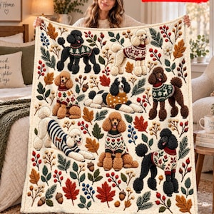 Peut inclure: Un plaid couleur crème orné d'un motif répétitif de caniches portant divers pulls à motifs, entremêlés de feuilles d'automne, de branches de pin, de baies rouges et de glands. Le texte 2D FLAT PRINTED apparaît dans le coin supérieur droit.