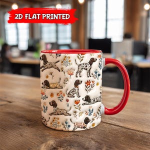 Może przedstawiać: Biały ceramiczny kubek z czerwonym wnętrzem i uchwytem. Kubek ma powtarzający się wzór brązowych i białych psów oraz kolorowych kwiatów. Tekst "2D FLAT PRINTED" znajduje się w czerwonym banerze u góry.