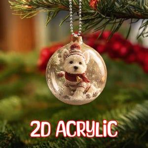 May include: A clear acrylic Christmas ornament featuring a small white dog wearing a red and white hat and scarf. The ornament has a silver chain for hanging and the text "2D ACRYLIC" in red.