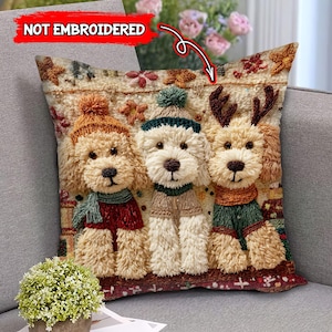 May include: A decorative pillow featuring three fluffy dog figures wearing winter attire. The dogs have hats, scarves, and sweaters in shades of brown, red, green, and cream. The pillow has a textured, embroidered appearance.