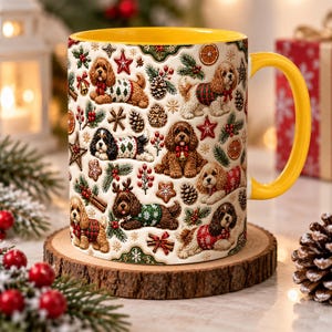 Könnte beinhalten: Ein Keramikbecher mit leuchtend gelbem Innenraum und Henkel, verziert mit einem wiederkehrenden Muster aus braunen und schwarzen Spaniel-Hunden in Weihnachtspullovern, zwischen Tannenzweigen, Tannenzapfen, roten Beeren und Sternen.