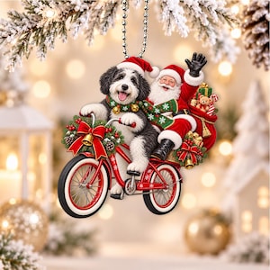 Könnte beinhalten: Ein hängender Weihnachtsbaumschmuck mit einem schwarz-weißen Hund, der eine Weihnachtsmütze und einen grünen Schal trägt und auf einem roten Fahrrad fährt. Der Weihnachtsmann sitzt winkend dahinter mit einem roten Geschenkesack.
