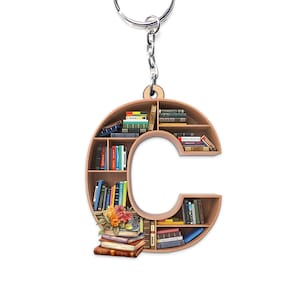 Puede incluir: Un llavero de madera con forma de letra C, con estanterías llenas de libros. El llavero tiene un anillo de llave plateado.