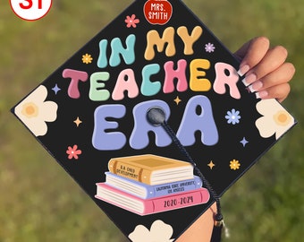 May include: A black graduation cap with the text "*IN MY TEACHER ERA*" in colorful, bubble-like letters. The cap also features a small red apple with the text "MRS. SMITH" and a stack of books with the text "CALIFORNIA STATE UNIVERSITY LOS ANGELES 2020-2024".