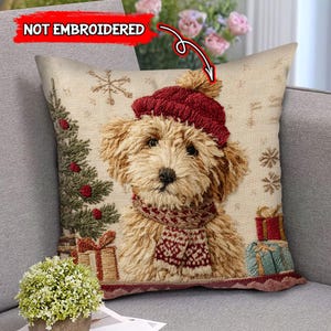Op de afbeelding: Een decoratief kussen met een hond met een rode gebreide muts en sjaal. Het ontwerp bevat een kerstboom, sneeuwvlokken en ingepakte cadeaus. De tekst "NOT EMBROIDERED" staat in de linkerbovenhoek.