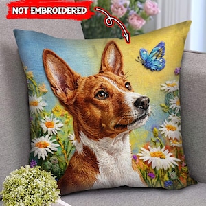 May include: A decorative throw pillow featuring a Basenji dog with brown and white fur, surrounded by daisies and a blue butterfly. The pillow has a yellow and blue background, with the text "NOT EMBROIDERED" in the upper left corner.