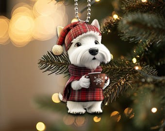 Può includere: Un cane West Highland White Terrier bianco con un cappello e una sciarpa a quadri rossi e neri, che tiene una tazza marrone con un fiocco di neve. Il cane è un ornamento natalizio.