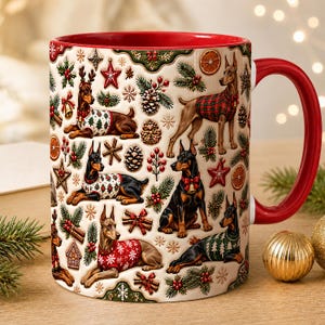 May include: A ceramic mug with a red interior and handle, featuring a cream-colored exterior decorated with a repeating pattern of Doberman dogs wearing holiday sweaters, pine cones, holly berries, stars, and dried orange slices.