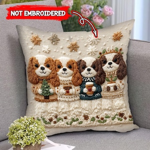 May include: Beige square pillow featuring an embroidered design of four Cavalier King Charles Spaniel dogs. Each dog is wearing a sweater and holding a festive item, such as a Christmas tree or a cup of coffee. The pillow has snowflake and floral accents.