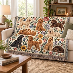 May include: A woven throw blanket featuring a cream background with a repeating pattern of various doodle-type dogs in shades of cream, gold, brown, and black, interspersed with colourful floral illustrations including sunflowers, tulips, and lavender.