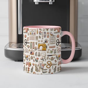 May include: A white ceramic mug with a light pink interior and handle, featuring a repeating pattern of sewing supplies including a yellow sewing machine, scissors, spools of thread, needles, thimbles, and small floral illustrations.