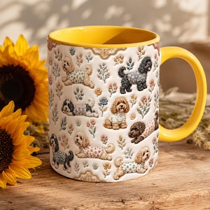 May include: A white ceramic mug with a bright yellow interior and handle, featuring a repeating pattern of small dogs wearing patterned shirts interspersed with colourful floral illustrations across the exterior surface of the vessel.