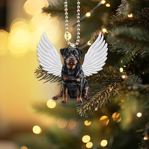 Può includere: Un cane Rottweiler nero e marrone con ali d'angelo bianche appese a una catena d'argento. Il cane indossa un'aureola bianca e ha un'espressione triste sul viso. Lo sfondo è un'immagine sfocata di un albero di Natale con luci.