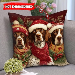 May include: A decorative throw pillow featuring three dogs wearing Santa hats and scarves. The dogs have brown and white fur and are set against a burgundy background with Christmas-themed accents. The text "NOT EMBROIDERED" is visible.