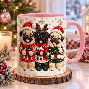 May include: A ceramic mug with a light pink interior and handle, featuring a raised 3D design of three pugs wearing holiday sweaters and hats. The center pug is black with reindeer antlers, while the two side pugs are fawn-colored with Santa hats.
