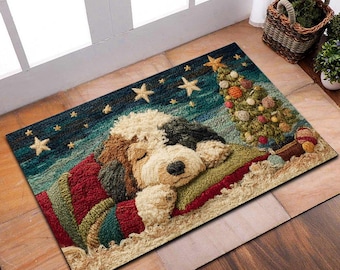 Puede incluir: Una alfombra rectangular con un perro durmiendo que lleva un suéter rojo y verde, con un árbol de Navidad y estrellas en el fondo. El perro es crema, marrón y negro. La alfombra está hecha de un material texturizado.
