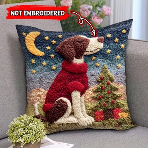 May include: A decorative throw pillow featuring a dog wearing a red sweater, sitting in front of a Christmas tree and presents. The background depicts a night sky with a crescent moon and stars. The text "NOT EMBROIDERED" is visible.