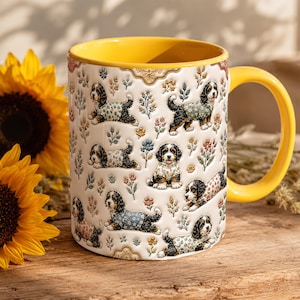 Op de afbeelding: Een keramische mok met een felgele binnenkant en handvat, met een gebroken witte buitenkant versierd met een herhalend patroon van kleine zwart-wit-bruine honden in truien met patronen, afgewisseld met kleurrijke bloemtakjes.