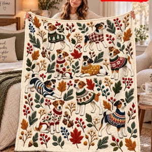 Peut inclure: Un plaid couleur crème orné d'un motif répétitif de terriers Jack Russell portant divers pulls à motifs, entremêlés de feuilles d'automne, de baies rouges, de branches de pin et de glands. Le texte 2D FLAT PRINTED est visible.