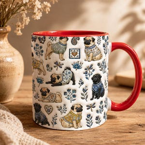 May include: A white ceramic mug with a bright red interior and handle, featuring a repeating pattern of pugs wearing patterned sweaters, interspersed with small blue floral motifs, dragonflies, butterflies, and heart-shaped decorative icons.