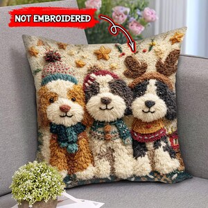 May include: A decorative square pillow featuring three dogs wearing winter attire. The dogs have brown, black, and white fur, and are wearing hats, scarves, and sweaters. The pillow has a textured appearance with star and antler accents. The text "NOT EMBROIDERED" is visible.