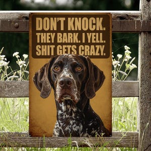 May include: A metal sign with a brown background and the text "DON'T KNOCK. THEY BARK. I YELL. SHIT GETS CRAZY." A German Shorthaired Pointer dog is featured below the text. The dog has brown and white markings and is looking at the viewer.