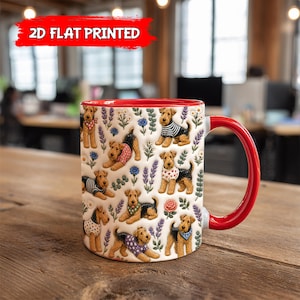 May include: A white ceramic mug with a red interior and handle, featuring a repeating pattern of Airedale Terrier dogs wearing various patterned sweaters and bandanas, interspersed with colorful illustrations of lavender and small flowers.