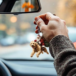 May include: A car charm featuring a Santa Claus figurine riding a golden retriever dog. The charm is hanging from a rearview mirror in a car.